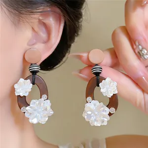 Gedetailleerd overzicht van elegante oorbellen met houten ringen en witte harsbloemen chic