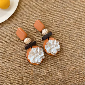 Detail van vintage oranje hangoorbellen met een delicaat parelmoerachtig bloemdesign