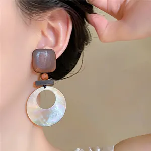 Detailweergave van retro geometrische oorbellen met houtstructuur en parelmoer ring.
