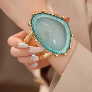 Nahaufnahme einer goldenen Manschette mit einem großen blaugrünen Harzstein-Schmuck.