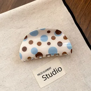 Detail view of a cream-colored hair claw clip featuring blue and brown polka dot patterns.