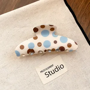 Detailed view of cream claw clip with blue and brown polka dots on a canvas background