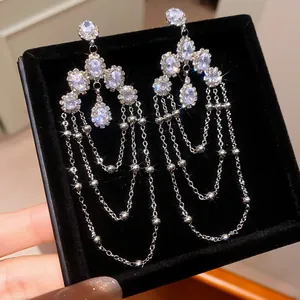Close-up detail of sparkling oval zircon dangle earrings with multi-layer chains.