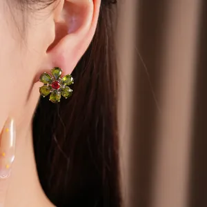 Nahaufnahme von Vintage-Blumenohrringen mit grünen und roten Zirkonsteinen am Ohr