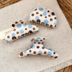 Detailed view of three polka dot hair claw clips in blue and brown on a linen surface