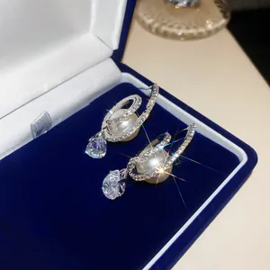Detail shot of elegant pearl and teardrop zircon pendant earrings in a blue jewelry box