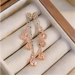 Macro detail of layered golden tassel earrings featuring faceted peach crystal pendants