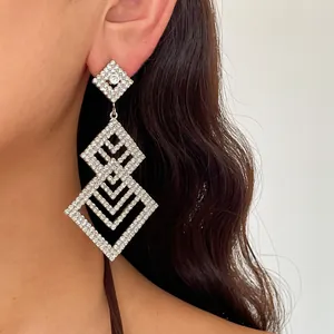 Detailaufnahme von eleganten, silbernen, geometrischen Strass-Ohrhängern am Ohr.