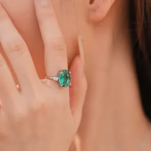 Close-up van elegante ovale groene zirkoon ring met fonkelende zijstenen aan de hand van een model.
