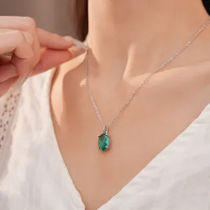 Elegante close-up van een zilveren ketting met groene zirkoon hanger gedragen door een model.