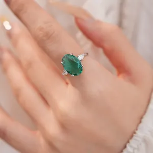 Elegante ovale smaragdgroene zirkoonring met zijstenen op handmodel detailweergave