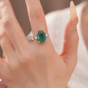 Close-up van een elegante smaragdgroene ovale zirkoon ring met zijstenen aan de vinger