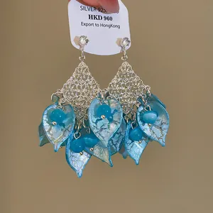 Detailweergave van boheemse blauwe acryl bloemblad oorbellen met glanzende zilveren knopjes.
