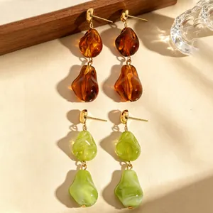 Detail van onregelmatige druppeloorbellen van hars in amber en groen met gouden metalen studs