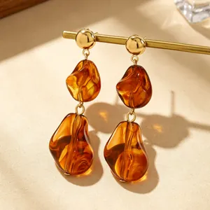 Detailopname van amberkleurige onregelmatige hars oorbellen met gouden knopjes op houder.