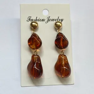 Detailopname van onregelmatige amberkleurige hars oorbellen met gouden knopjes.