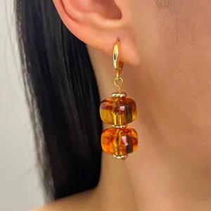Gedetailleerd overzicht van amber hars oorbellen met dubbele kralen en gouden ringen