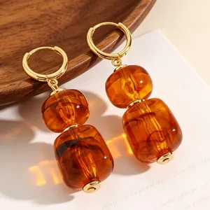 Detailopname van amberkleurige hars oorbellen met gouden ringen in sfeervol warm licht