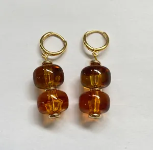 Detailopname van Maillard-oorbellen met amberkleurige harskralen en gouden ringen.