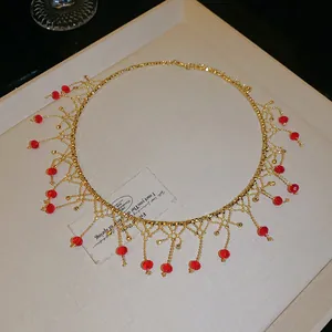 Gros plan d'un collier choker doré élégant avec des franges en cristal rouge et pompons
