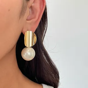 Detailansicht eines goldenen geometrischen Ohrsteckers mit einer großen cremefarbenen Perle