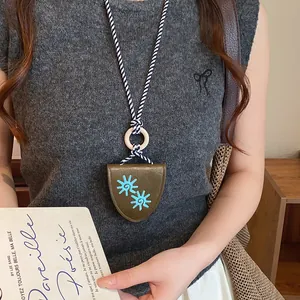 Détail du collier pince à lunettes en cuir tournesol rétro sur un pull en tricot gris