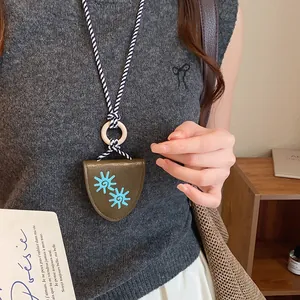 Détail d'un collier porte-lunettes rétro en cuir avec tournesol porté sur un pull gris.