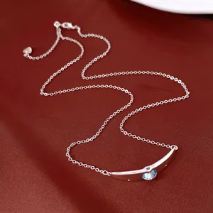 Dettaglio di una collana argentata con pendente curvo e una pietra azzurra luminosa.