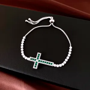 Bracelet croix argenté ajustable avec zircons verts et blancs sur fond noir.