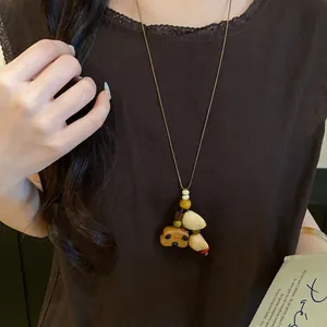 Close-up detail of retro ethnic pendant necklace with wood bear and shell charms on model.
