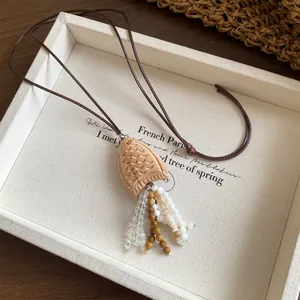 Detailed view of a vintage wooden fish pendant featuring shell bead tassels on a dark cord