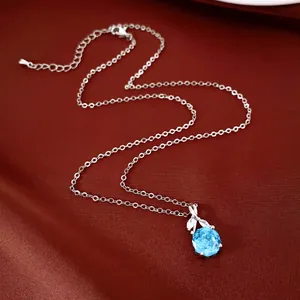 Detailopname van een zilveren ketting met een helderblauwe zirkonia bloemhanger op roode zijde.