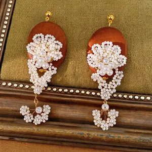 Close-up of vintage earrings featuring oval wood and intricate white pearl flower beadwork