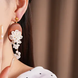 Close-up of oval wooden earrings featuring intricate pearl bead floral design and tassels