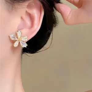 Gros plan d'une élégante boucle d'oreille fleur dorée avec perle et zircon sur l'oreille