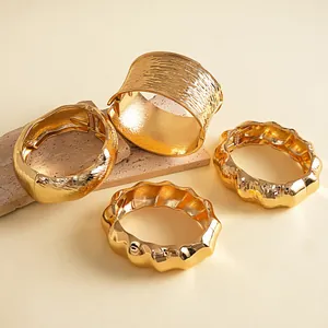 Detail van vier dikke gouden metalen armbanden met golf- en geplooide texturen. (83 chars)