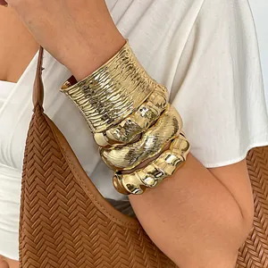 Dichtbij opname van gouden chunky metalen armbanden met geplooide en golvende textuur op arm
