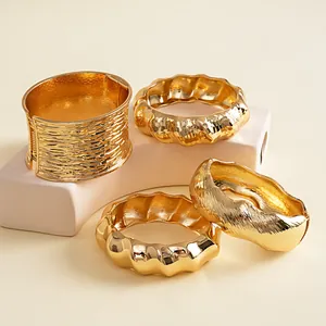 Detailweergave van vier goudkleurige metalen armbanden met rimpel- en golfstructuur.