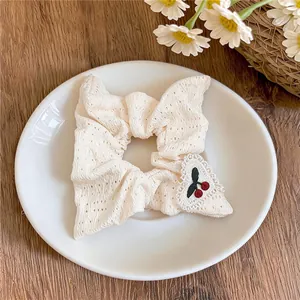Gros plan d'un chouchou en dentelle blanche avec un joli patch cœur brodé cerise.