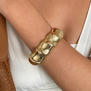Detailopname van een grove gouden manchetarmband met golftextuur gedragen om de arm van een model.