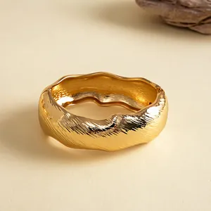 Detail van een grove gouden armband met een unieke golvende rand en geplooide textuur
