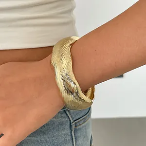 Gedetailleerde weergave van een trendy gouden golvende manchetarmband met geplooide textuur