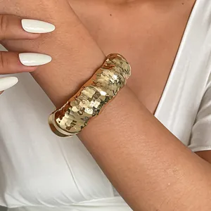 Detailopname van een dikke gouden metalen armband met een gegolfde gehamerde textuur.