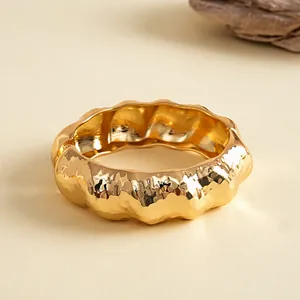 Detail van een gegolfde goudkleurige armband met een unieke kreukelmetaaltextuur.
