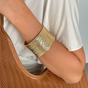 Gedetailleerde macro-weergave van een goudkleurige brede armband met golftextuur op de arm.