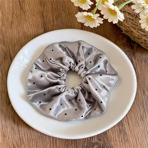 Détail d'un chouchou en satin gris à pois présenté sur une assiette blanche.