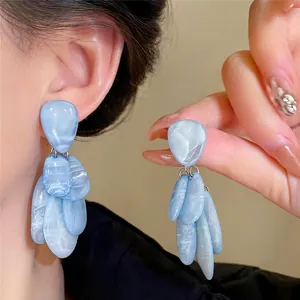 Pendientes colgantes de resina jaspeada azul hechos a mano mostrados en oreja y mano