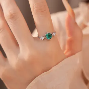 Detailopname van een zilveren ruitvormige ring met een groene zirkoon op een vinger