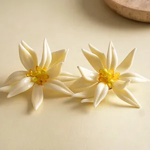 Detailansicht von handgefertigten Blumenohrringen aus cremefarbenem Harz und Kristall.
