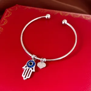 Détail d'un bracelet jonc argenté avec charms main de Fatma et cœur sur boîte rouge